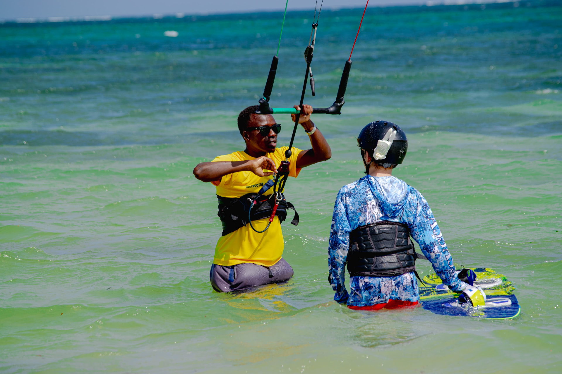Instructor helping a student with a kite bar in clear turquoise water